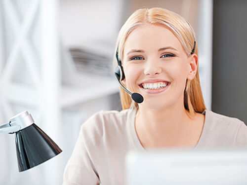 Happy young woman in headset looking at camera and smiling while sitting at her working place Happy young woman in headset looking at camera and smiling while sitting at her working place